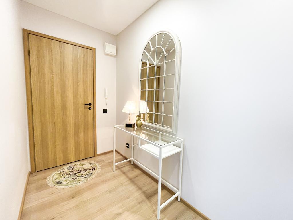 Valgusküllane esik koos valge konsoollaua ja kaarja peegliga, puidust uksed.
