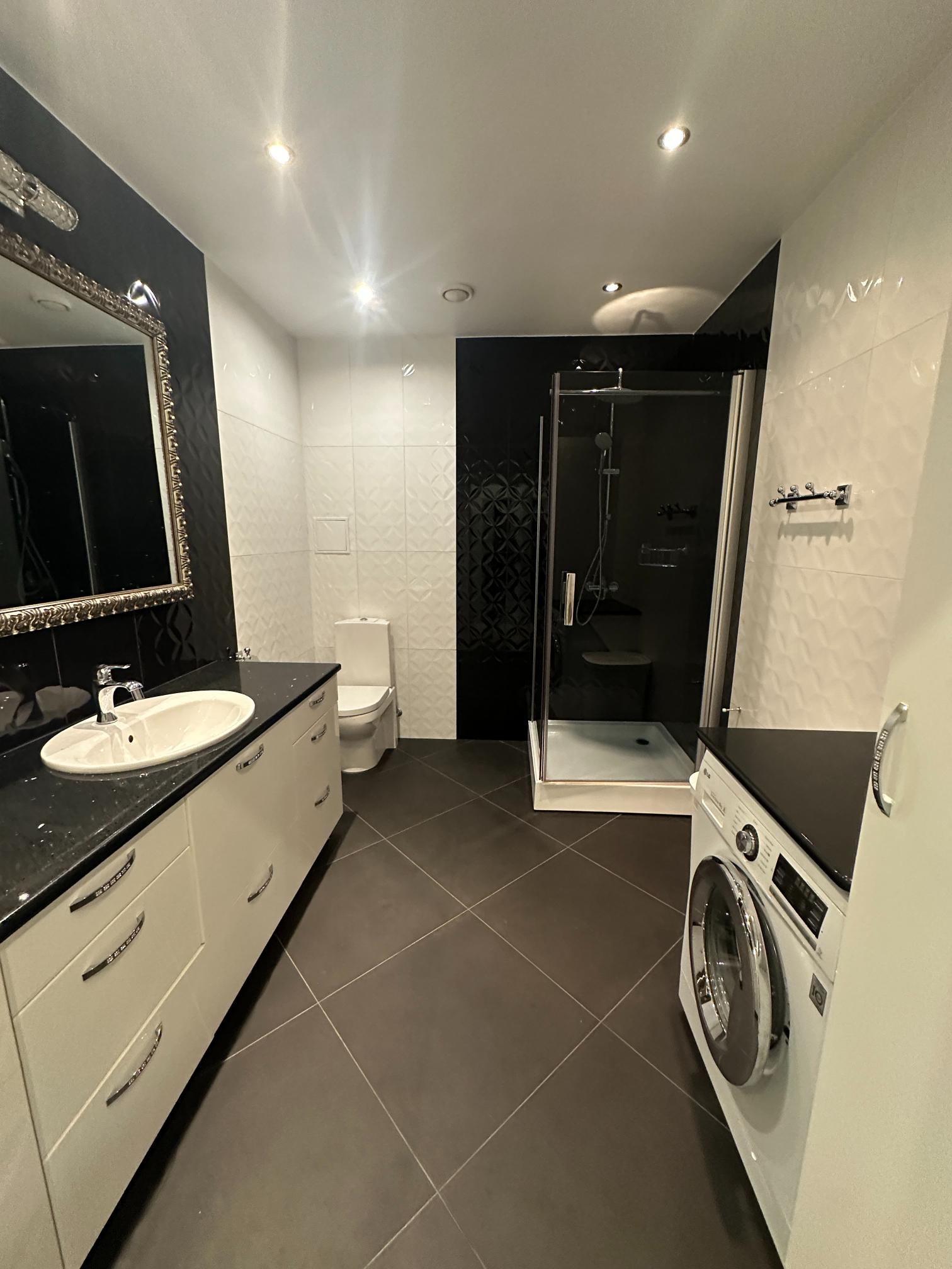 Moodne vannituba, varustatud dušinurga, pesumasinaga ja elegantse valamukapiga.