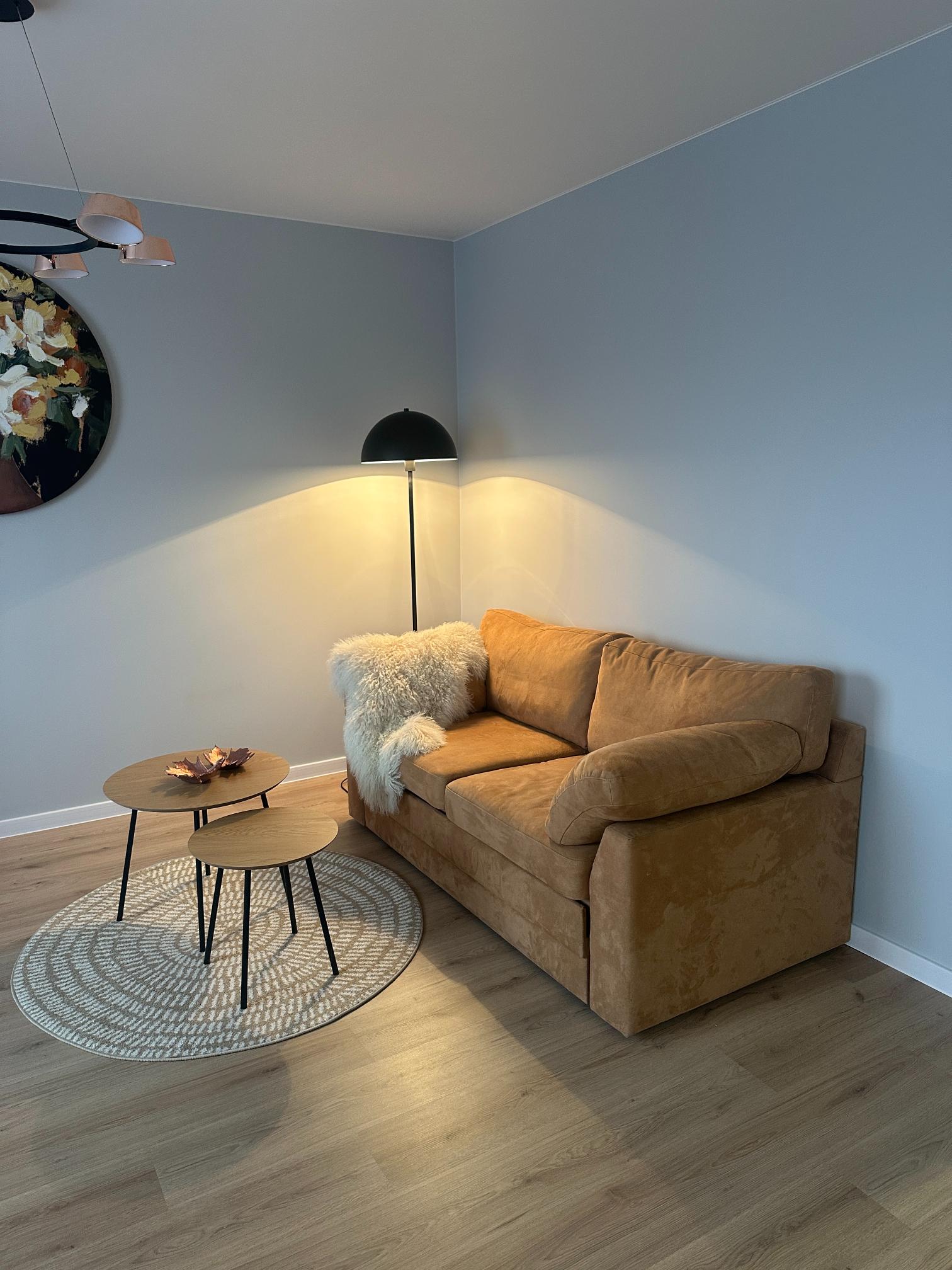 Stiilne elutuba pruuni diivani ja kahe ümmarguse lauaga. Soojalt valgustatud ruum.