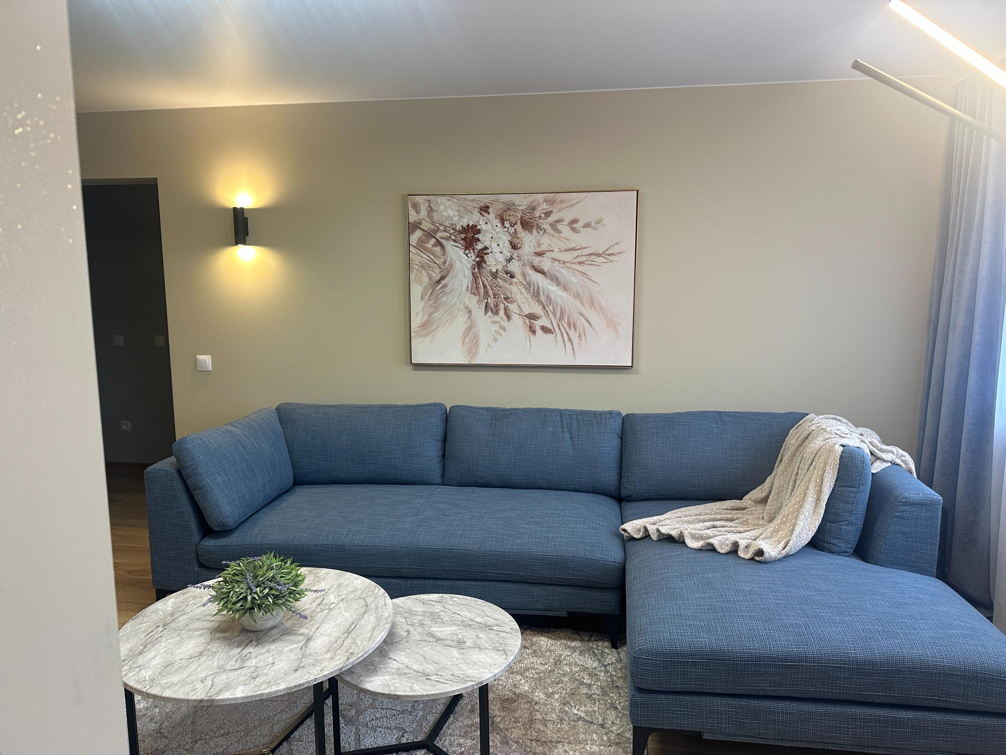 Avar elutuba sinise nurgadiivani, marmorist laua ja dekoratiivse kunstiteosega seinal.