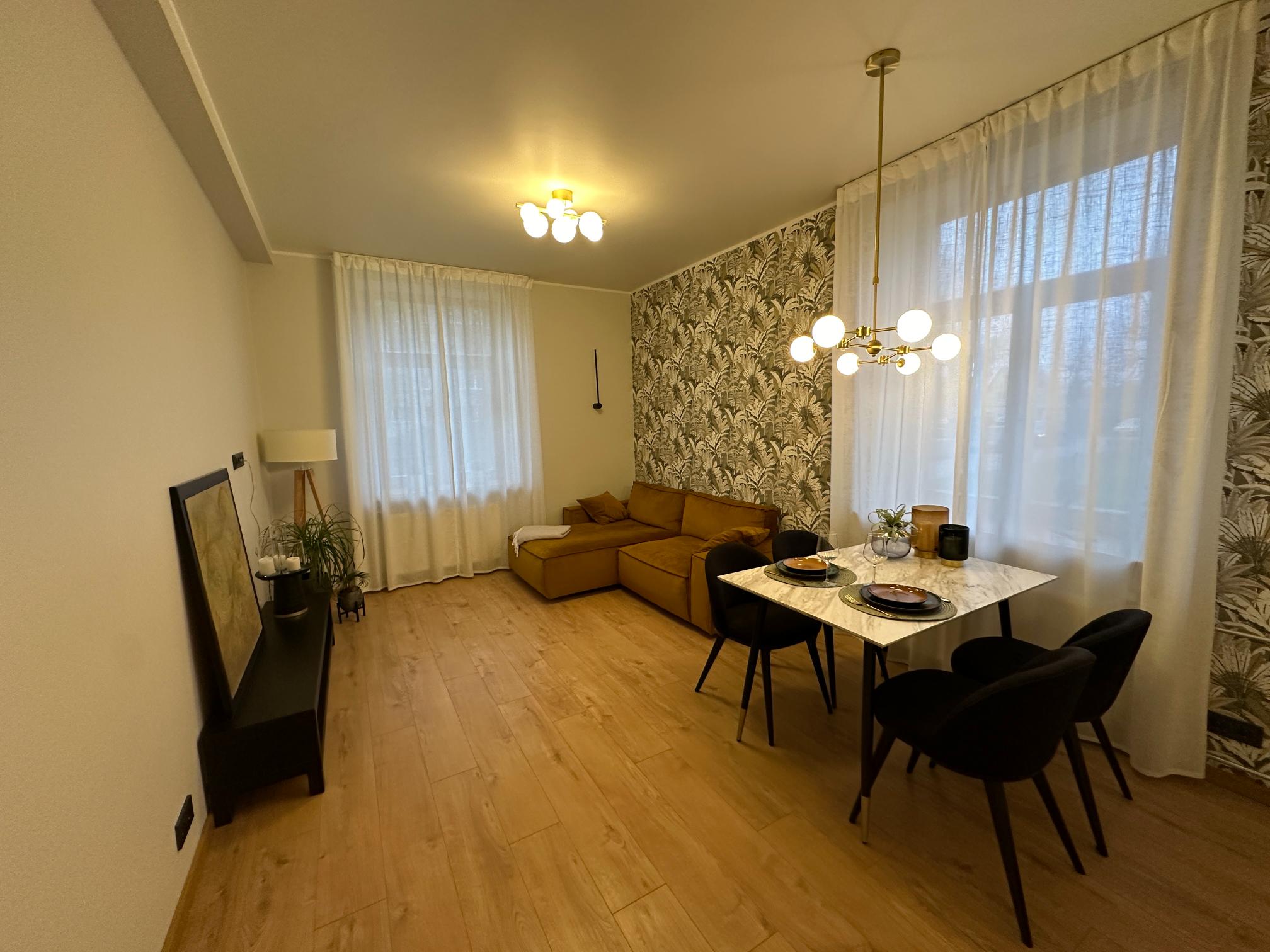 Valgusküllane elu- ja söögituba, kus on kollane diivan, laud ja elegantselt kaunistatud seinaga.