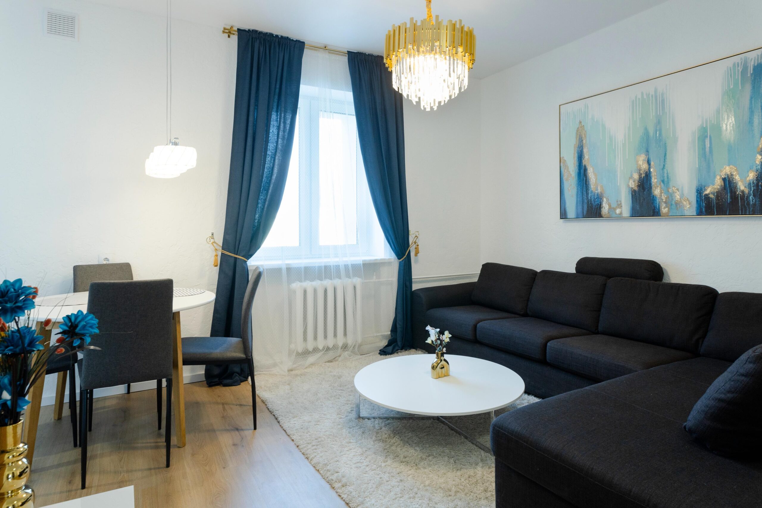 Elegantne elutuba siniste kardinatega, suur must diivan, kuldne lühter ja kaunis abstraktne maal.