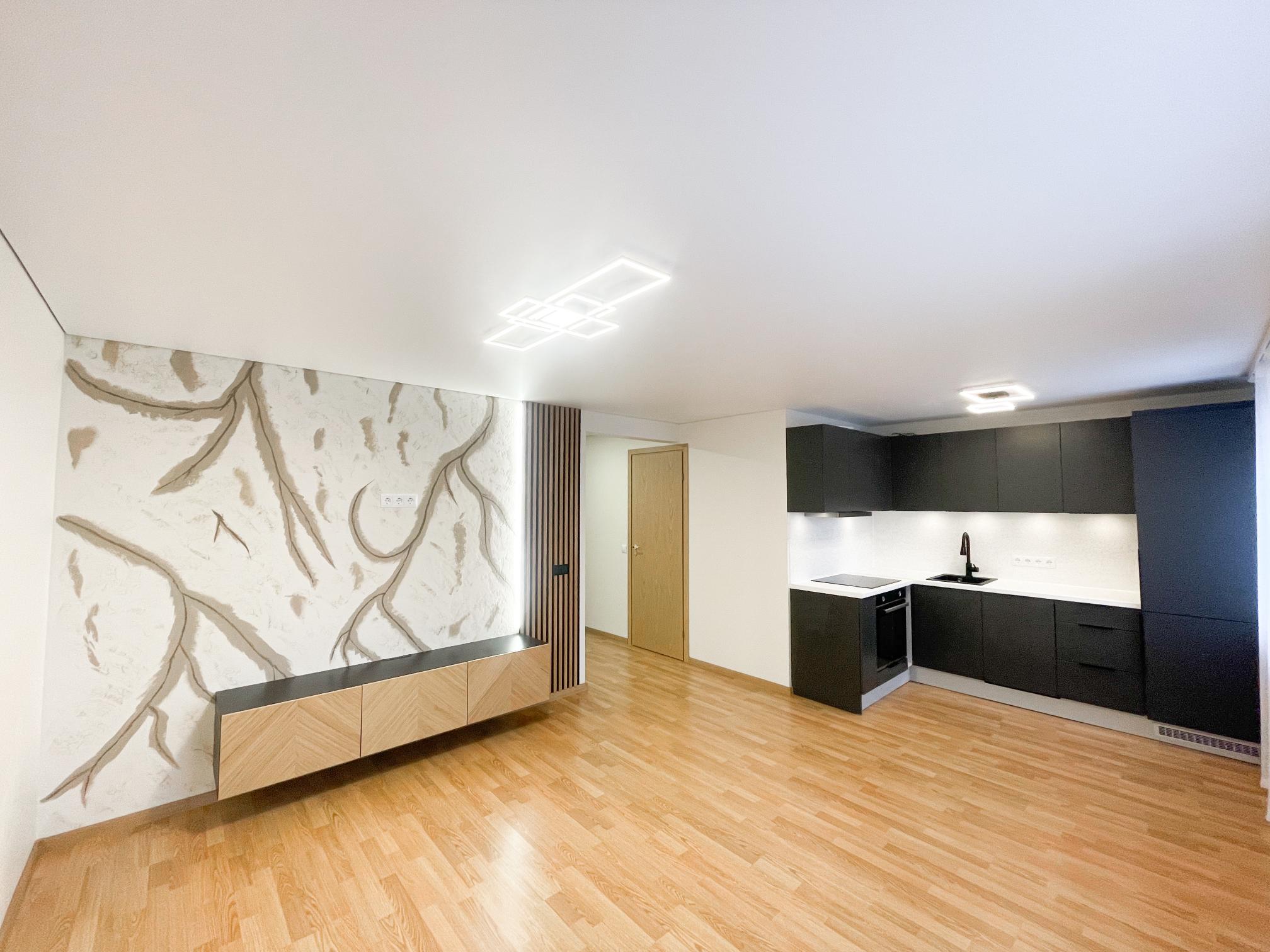 Modernne köök ja elutuba mustade köögikappide, abstraktse seina ja puitpõrandaga.