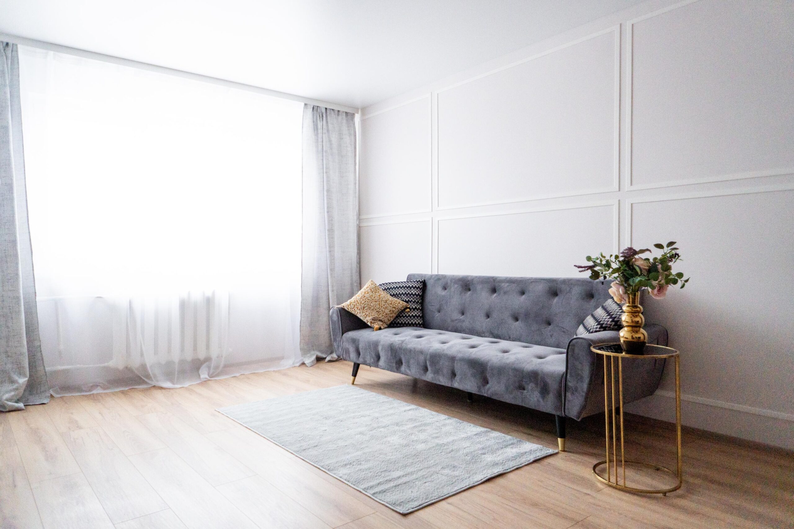 Minimalistlik elutuba Ida-Virumaa korteris. Hall sametdiivan, hele vaip ja kuldne abilauake dekoratiivvaasiga.